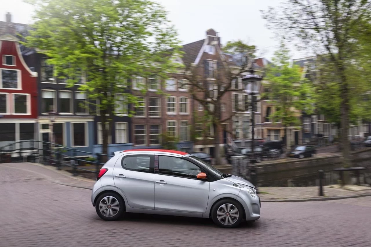 Vista lateral del Citroën C1 en un contexto urbano, resaltando su diseño compacto.