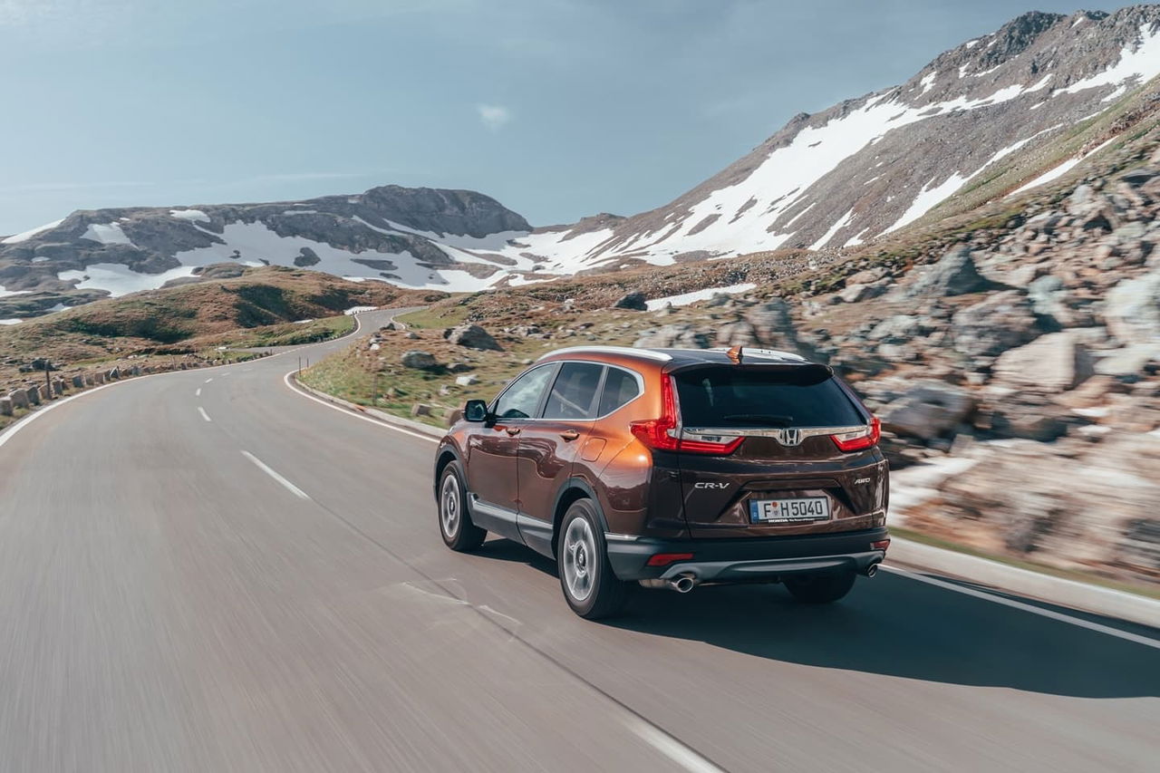 Vista dinámica de Honda CR-V en carretera de montaña, mostrando diseño trasero y lateral.