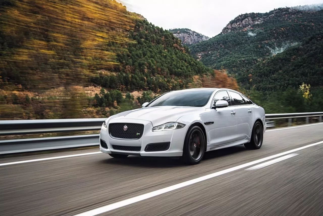 Vista delantera y lateral de un Jaguar XJ blanco en carretera de montaña.