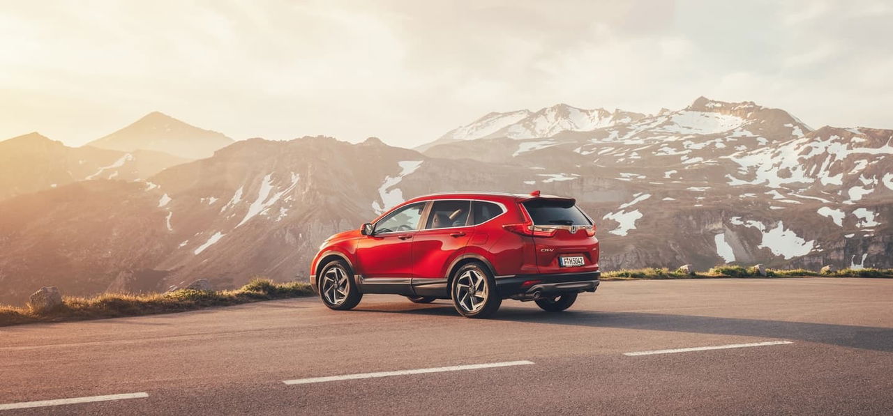 Honda CR-V en color rojo mostrando su perfil lateral contra paisaje montañoso.