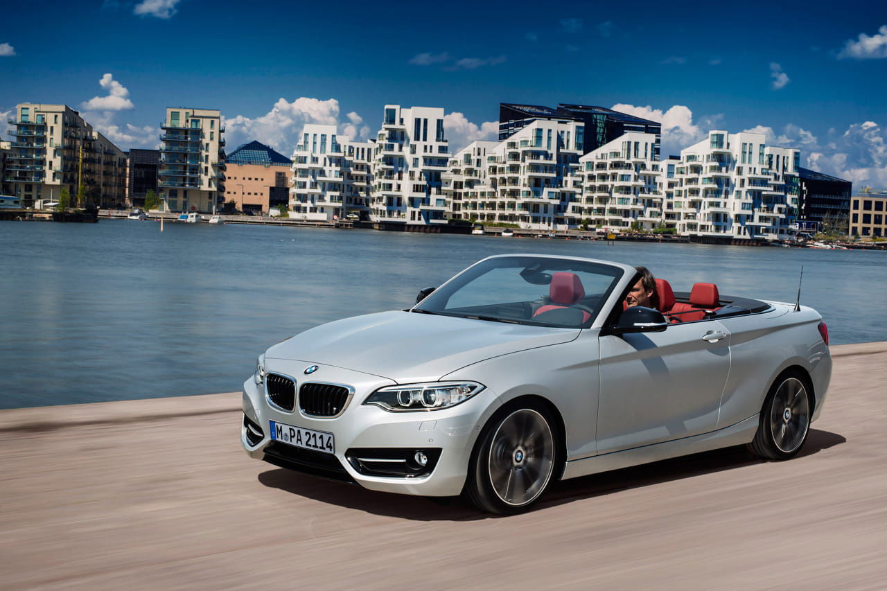 BMW Serie 2 Cabrio en vista delantera lateral, con el techo abajo y un fondo urbano.