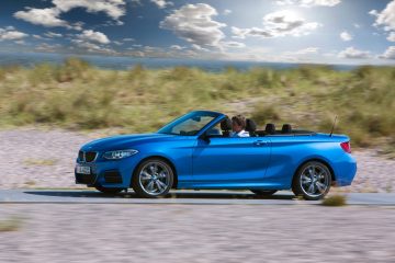 Vista lateral del BMW Serie 2 Cabrio con capota bajada en escenario costero.