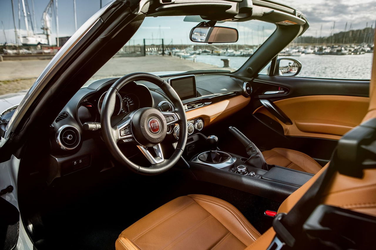 Elegante cabina del Fiat 124 con acabados en cuero marrón y volante deportivo.