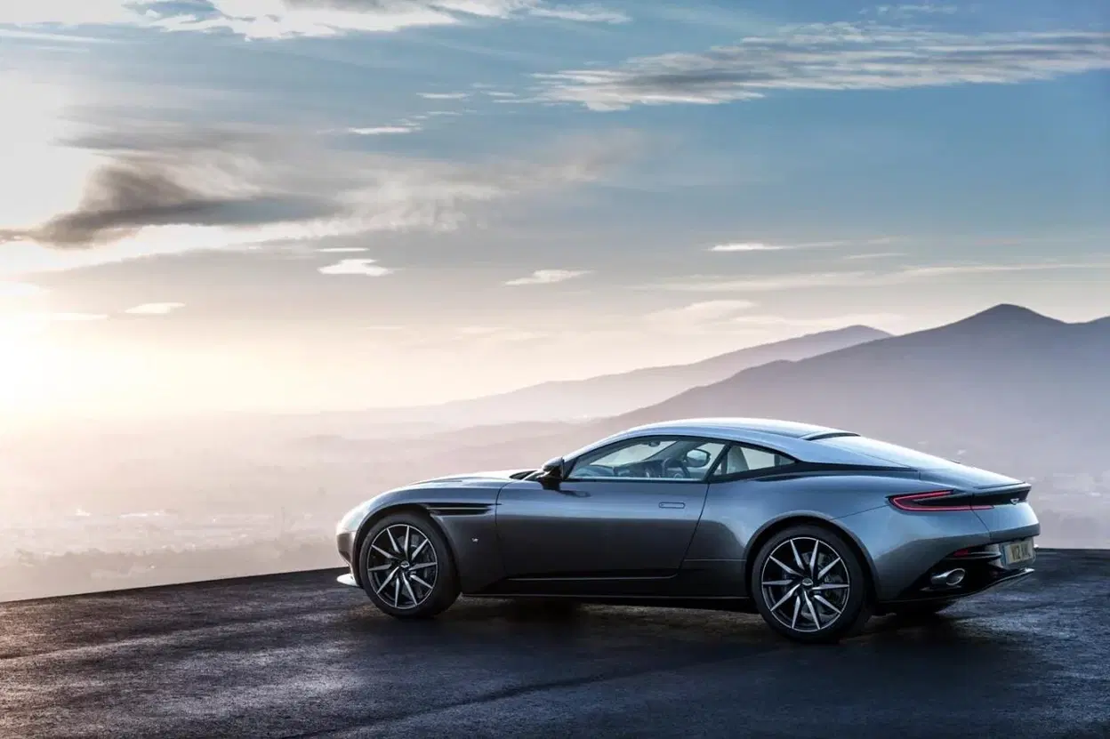 Vista lateral del Aston Martin DB11 posando sobre asfalto con montañas al fondo.