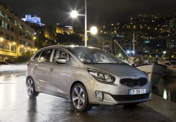 Kia Carens iluminado por la ciudad nocturna, mostrando su diseño lateral.