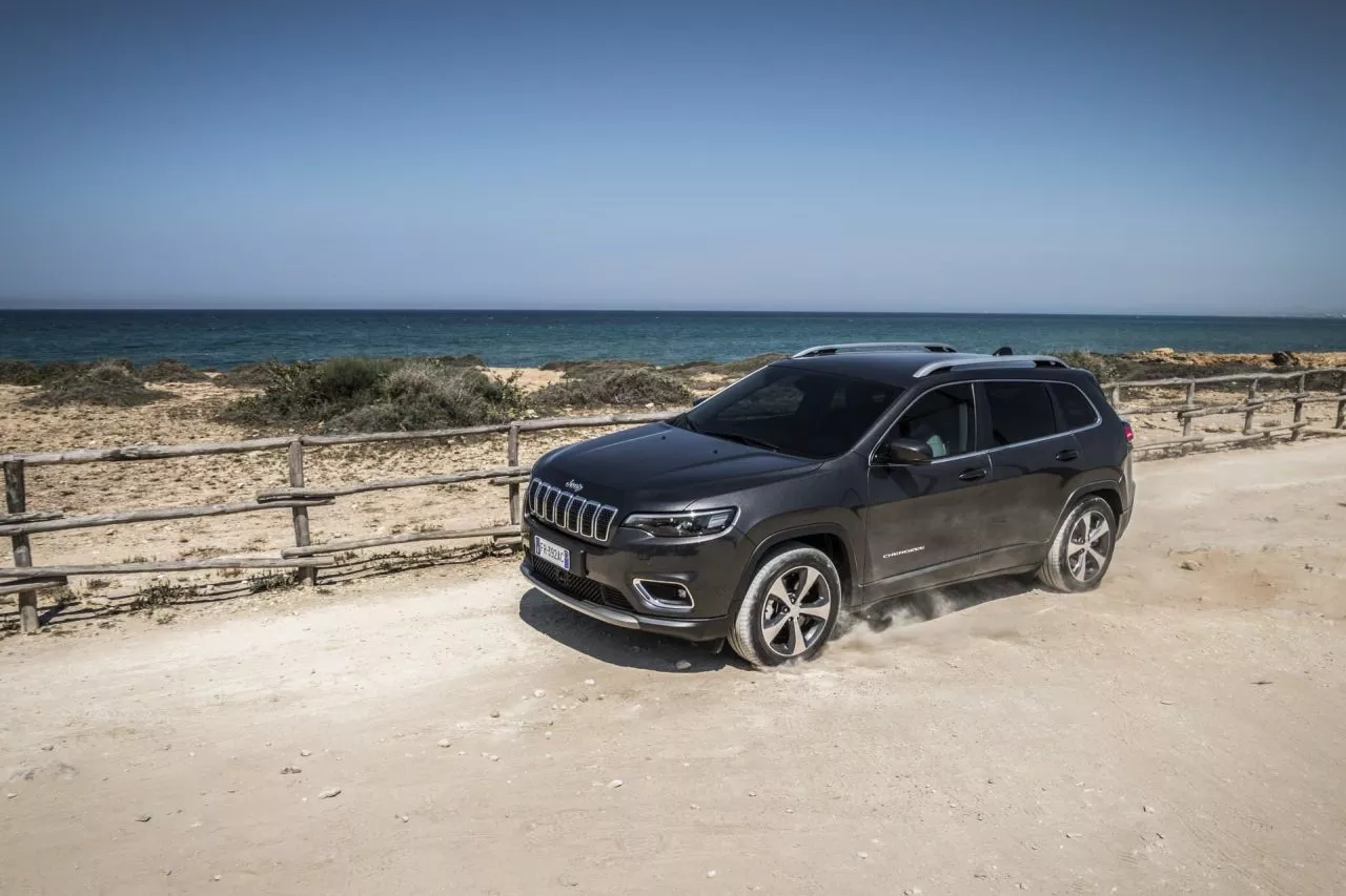 Vista lateral del Jeep Cherokee en una playa, mostrando su perfil y diseño de llantas.