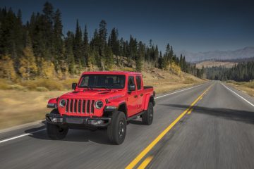 Vista lateral del Jeep Gladiator en color rojo circulando por carretera con paisaje montañoso.