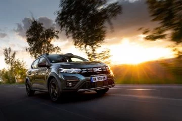 Vista dinámica del Dacia Sandero con el nuevo logo en plena ruta al atardecer