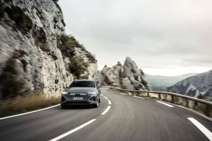 Audi Q8 e-tron captado en ruta montañosa, perspectiva frontal y lateral.