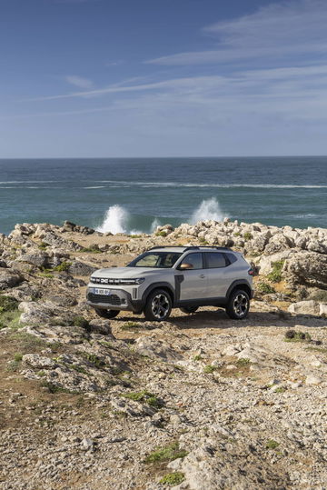 Vista lateral del Dacia Duster sobre terreno rocoso con el mar de fondo.