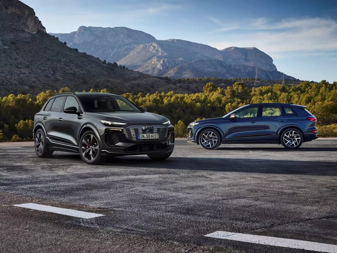 Dos variantes del Audi Q6 e-tron perfilados con montañas de fondo.