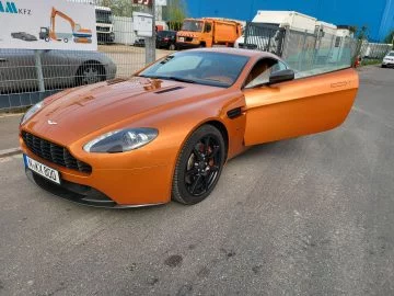 Un Aston Martin en tono naranja con la puerta abierta, mostrando su perfil imponente.