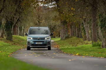 Vista frontal lateral del Citroën Berlingo avanzando por un camino rodeado de vegetación.