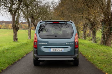 Vista trasera del Citroën Berlingo rodando por un camino rodeado de verde.