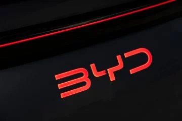 Emblema rojo iluminado de BYD sobre fondo negro, detalle de calidad y diseño.