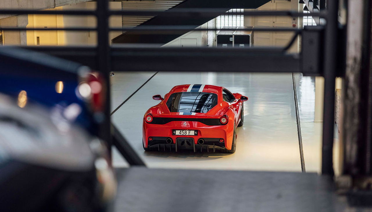 Vista trasera y lateral de un Ferrari rojo en el interior de un garaje iluminado.