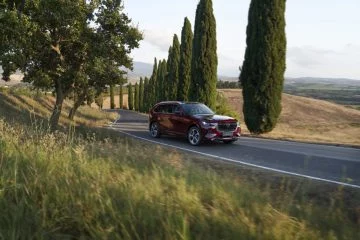 Vista dinámica del Mazda CX-80 2024 en rojo Artisan atravesando una carretera serpenteante.