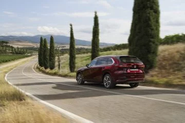 Vista dinámica de la trasera y lateral del Mazda CX-80 2024 en movimiento.