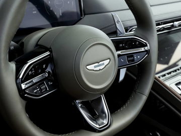 Detalle del volante del Aston Martin con vistas a su emblema sobresaliente y comandos de control.