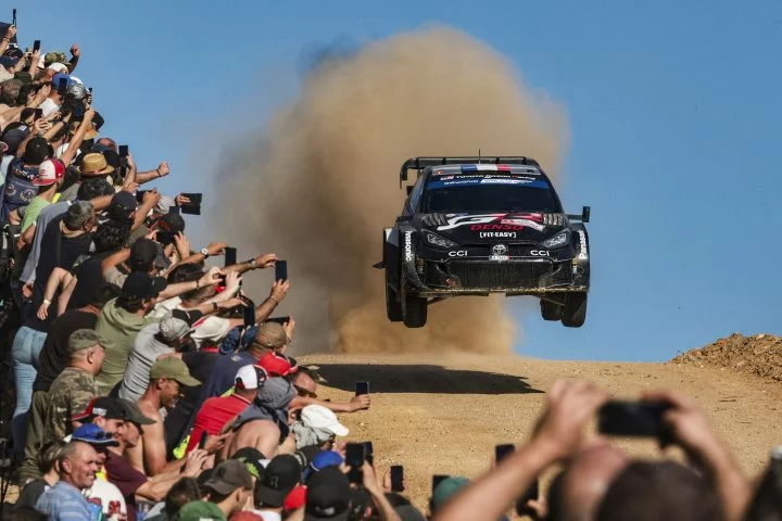 Vistazo dinámico del rally con el coche de Ogier en pleno salto, levantando polvo y emociones.