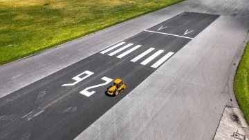 Vista aérea de un vehículo amarillo desplazándose en una pista de asfalto, demuestra diseño aerodinámico.