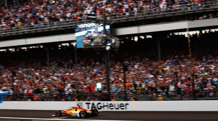 Imagen dinámica de Josef Newgarden compitiendo en Indy 500 con el equipo Penske.