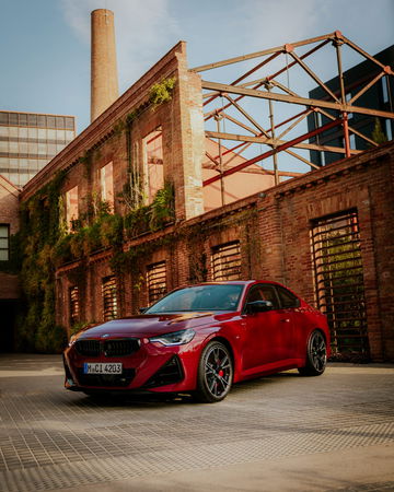 Renovado BMW M240i xDrive coupé en rojo vibrante, vista lateral y frontal.