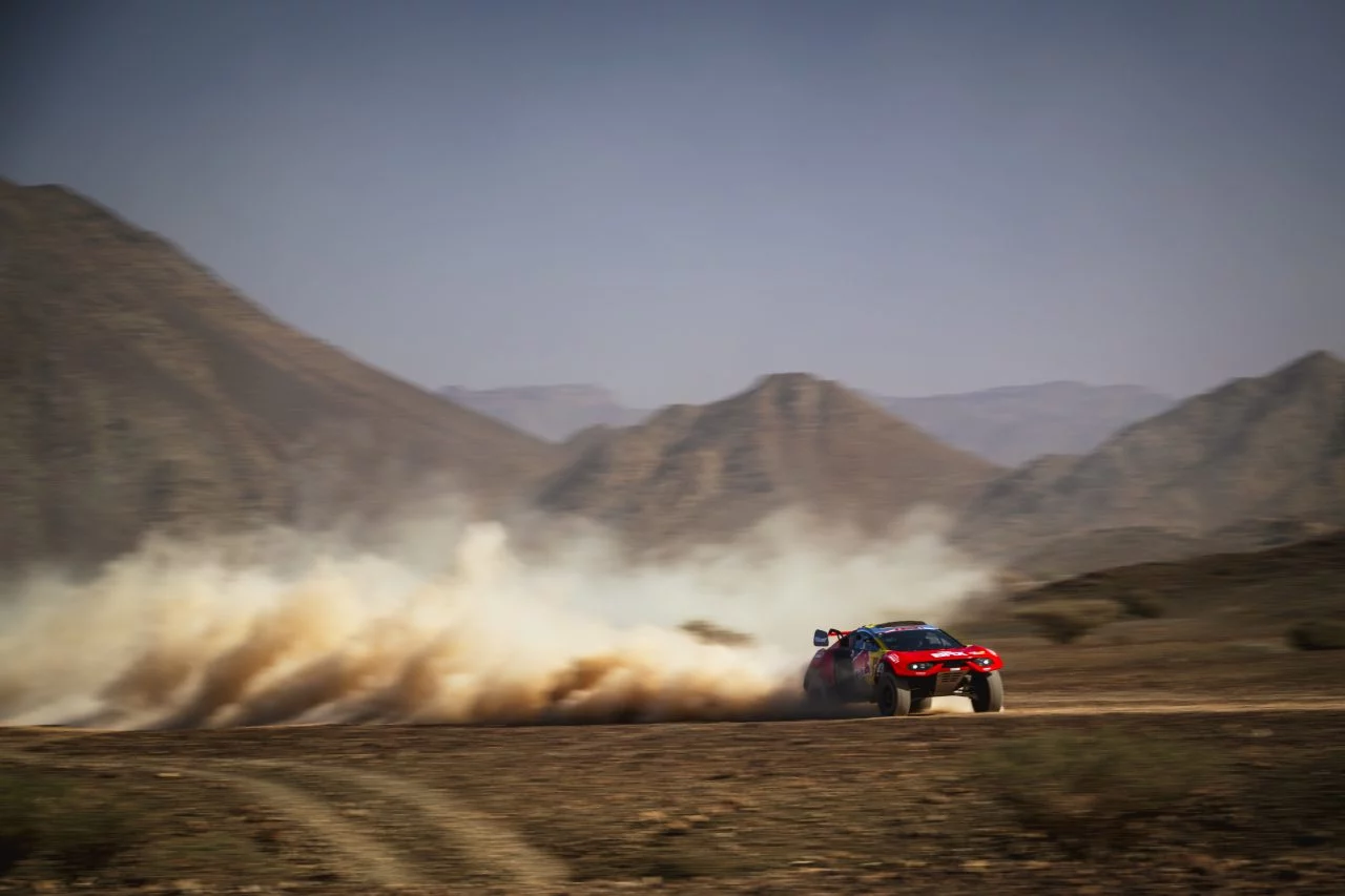 Vehículo compitiendo en el árido paisaje saudí, levantando una estela de polvo.