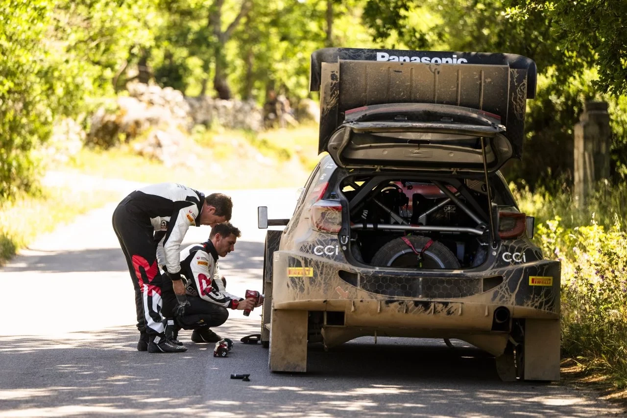 Imagen de un equipo de rally inspeccionando la parte trasera del vehículo, posible análisis de daños.