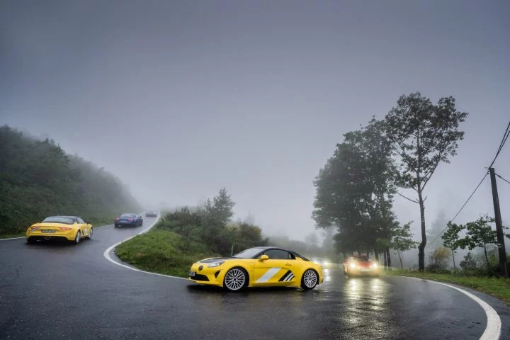 Alpine amarillo capturado en plena curva bajo condiciones húmedas, reflejando su dinámica ágil.
