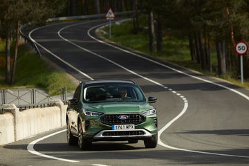 Vista dinámica del Ford Kuga 2024 en carretera serpenteante, mostrando su línea lateral y frontal.