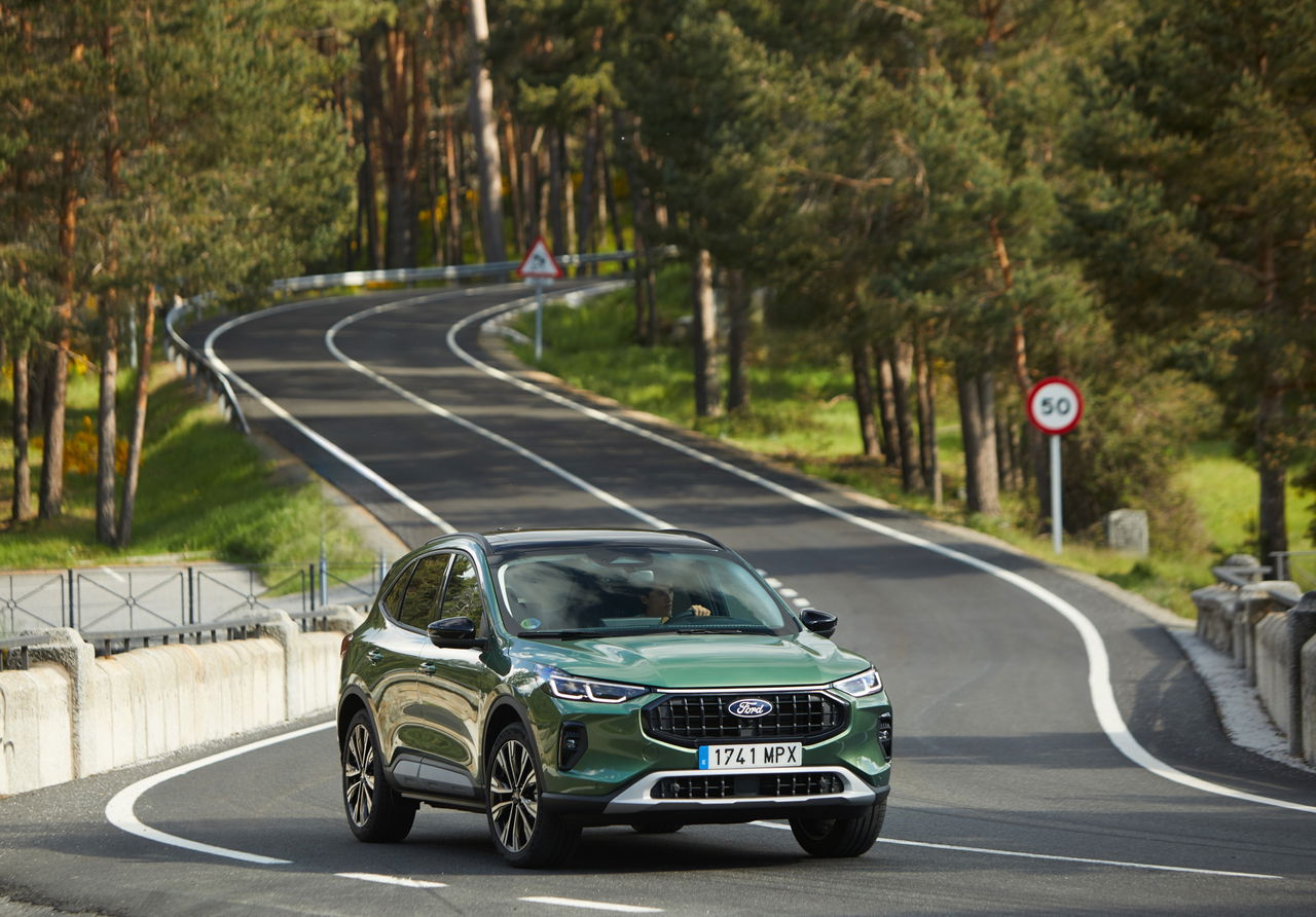 Vista dinámica del nuevo Ford Kuga 2024 mientras recorre una carretera entre bosques.