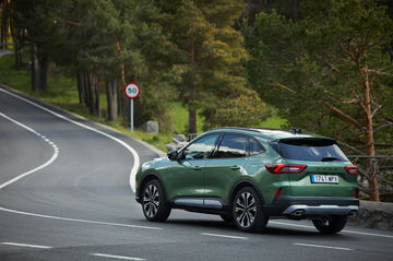 Vista lateral del Ford Kuga 2024 en carretera con paisaje verde al fondo.