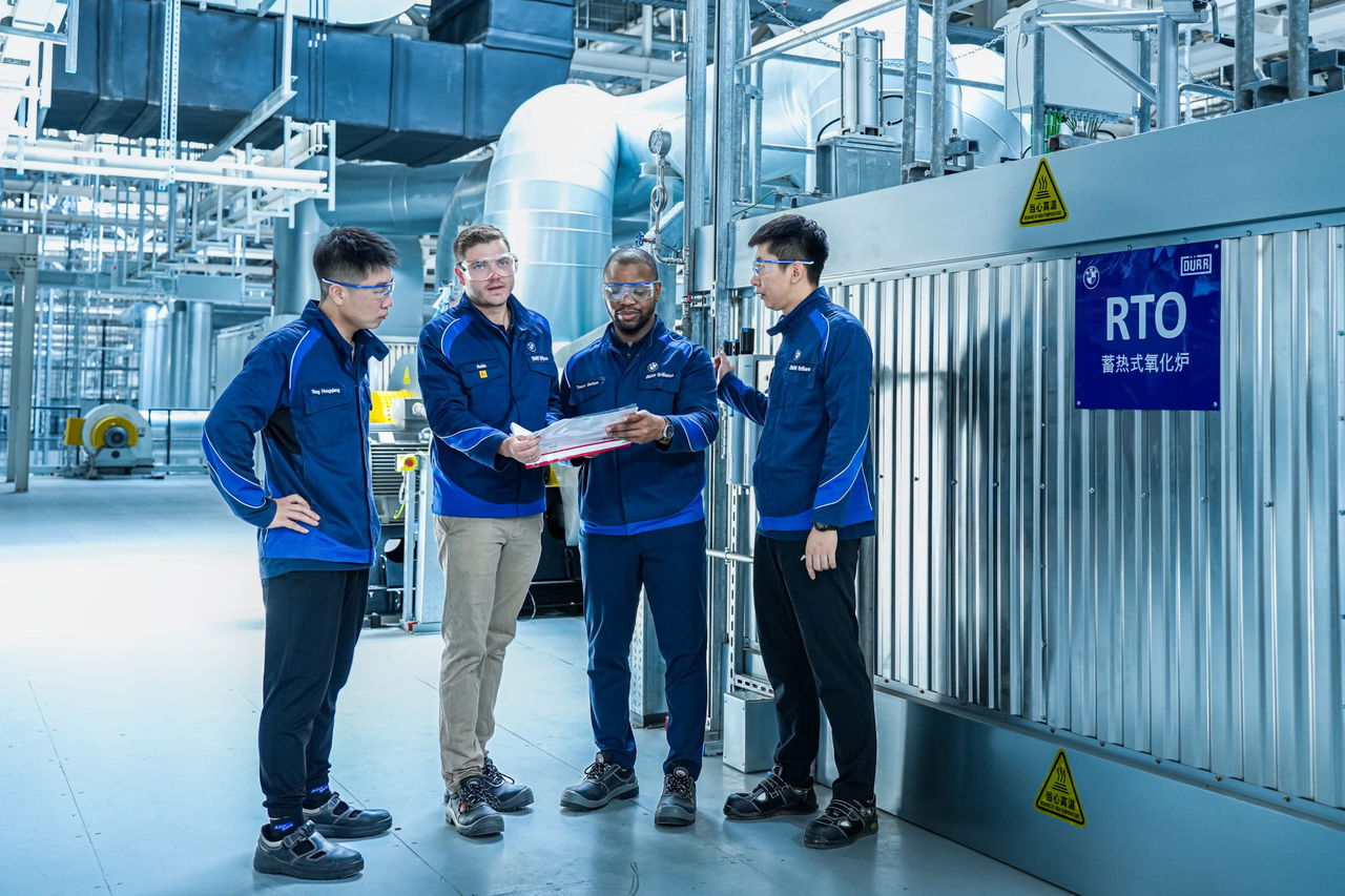 Grupo de ingenieros de BMW discutiendo sobre planos en una instalación industrial.