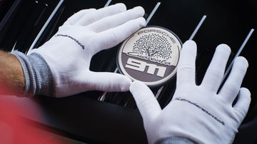 Moneda conmemorativa del 40º aniversario de Porsche Ibérica junto a un guante blanco.