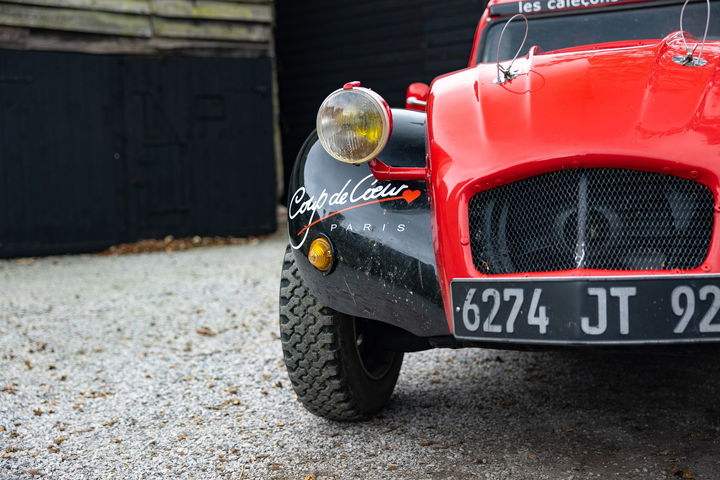 Vista parcial de un Citroën 2CV rojo preparado para rally, enfocando en su frontal