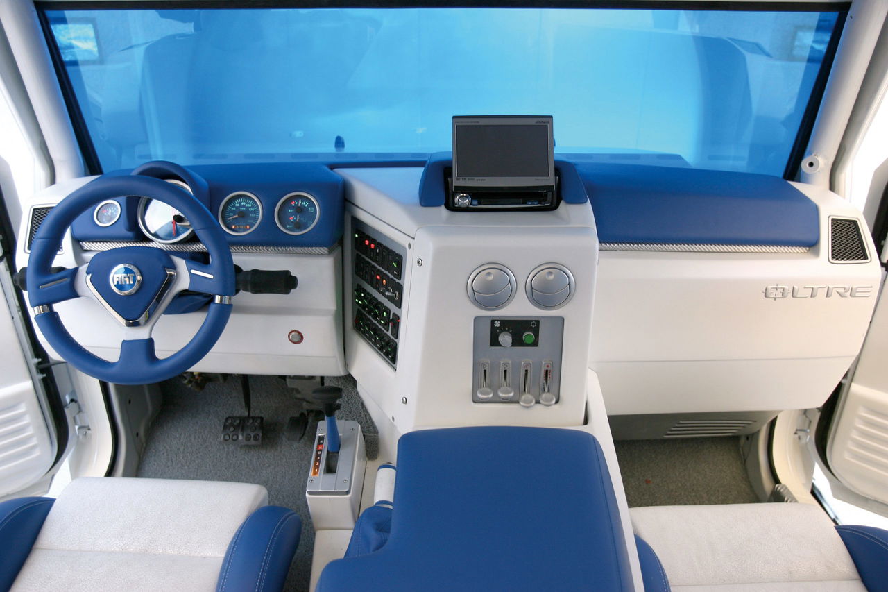 Interior del Oltre Fiat con volante y asientos en tonos azules, panel central con pantallas.