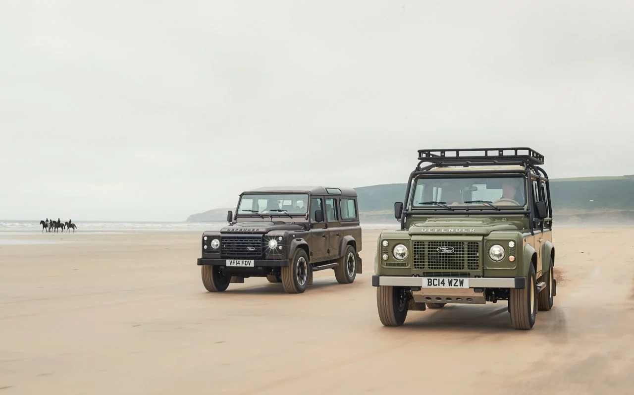 Dos modelos del Land Rover Defender clásico en la playa, potencia y estilo retro.