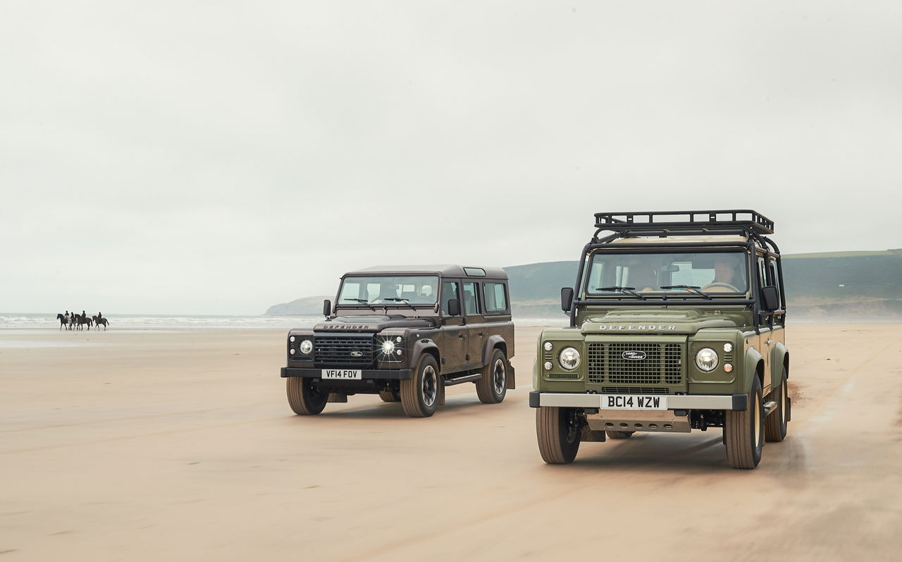 Dos modelos del Land Rover Defender clásico en la playa, potencia y estilo retro.