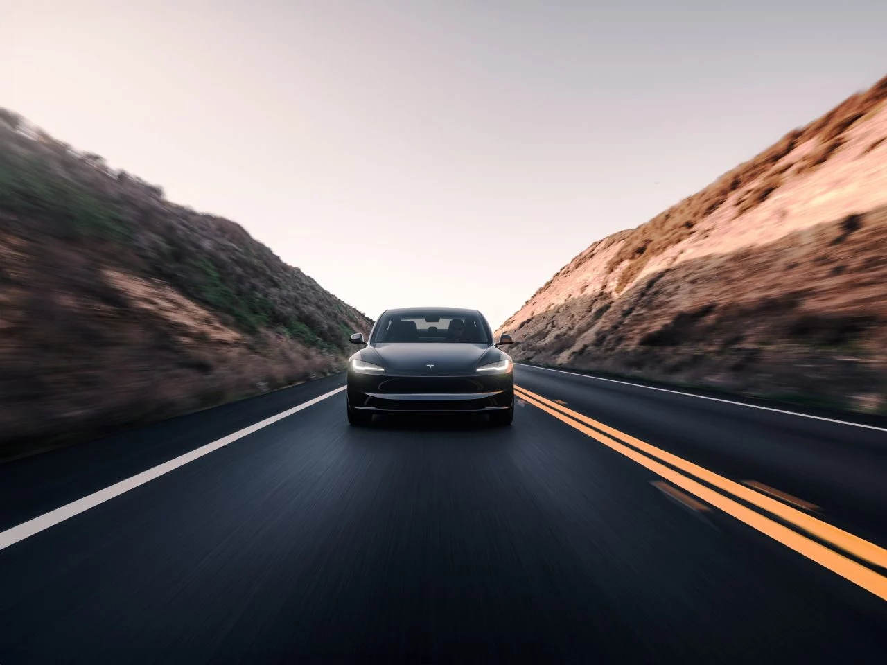 Vista frontal del Tesla Model 3 en movimiento, capturando su esencia aerodinámica.