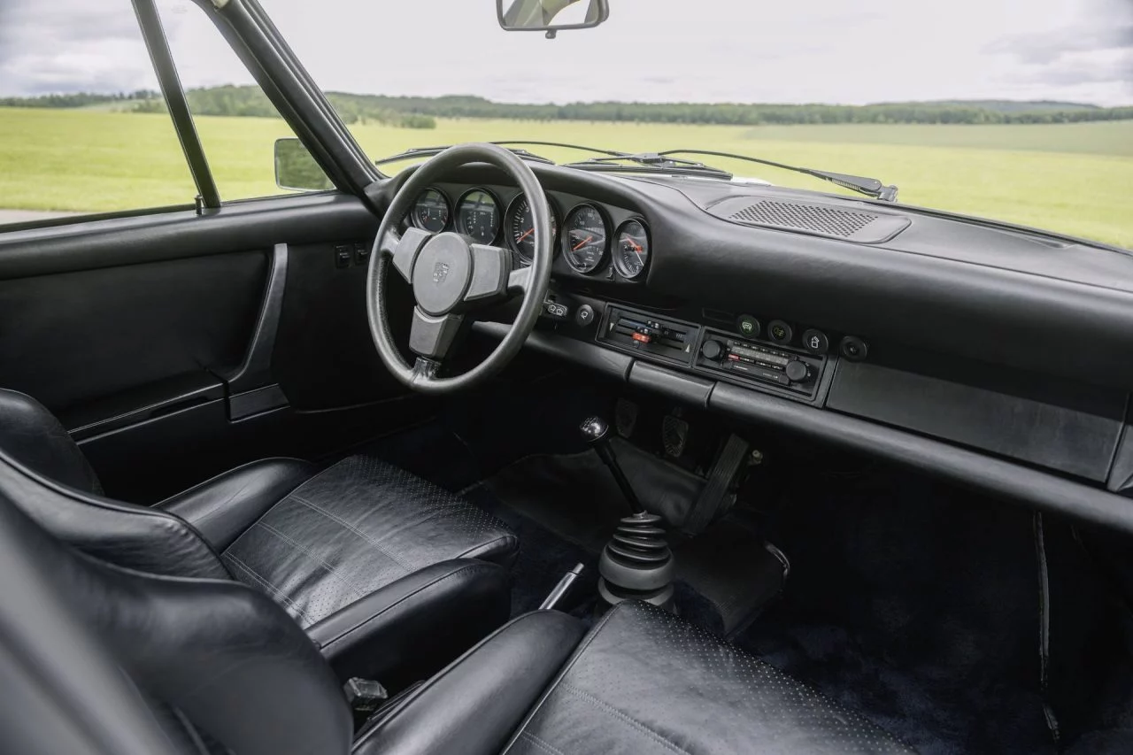 Clásico habitáculo Porsche con asiento de cuero y volante icónico.