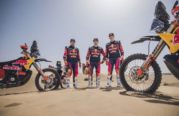 Pilotos KTM junto a motocicletas de competición en el desierto.