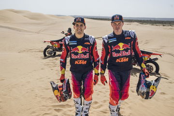 Pilotos KTM posan junto a motos de rally en dunas de Marruecos