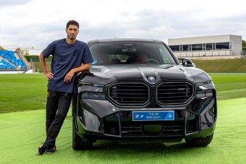 Jugador apoyado en la delantera un BMW, mostrando el diseño y potencial del vehículo.