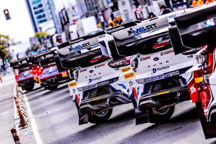 Colas de WRC híbridos alineados en parque de servicio, destacando aerodinámica.