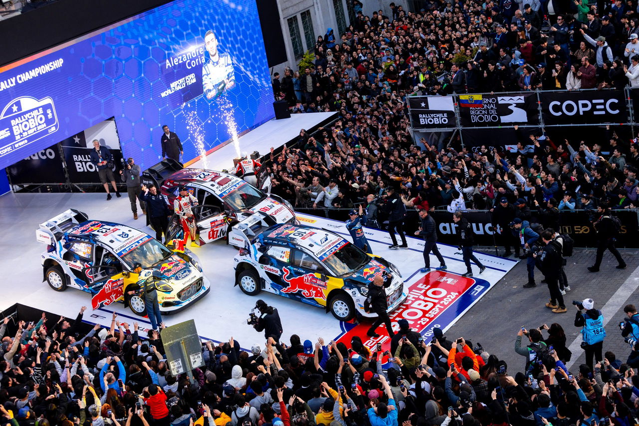 Dos vehículos de rally compitiendo y público celebrando en la ceremonia de inicio.