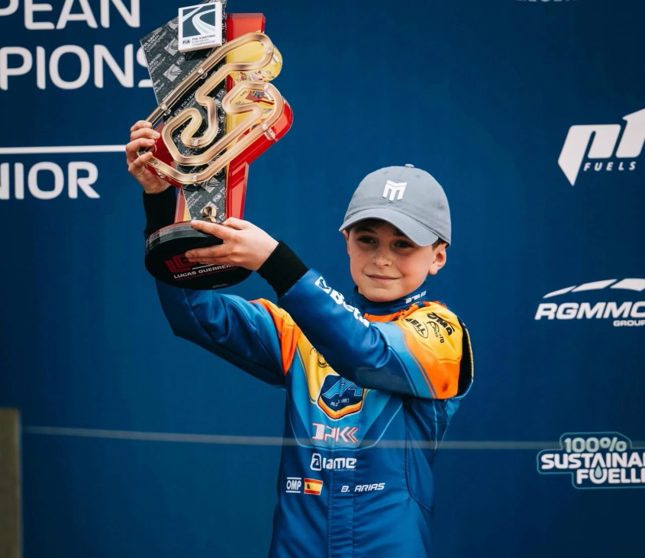 Bosco Arias celebra una victoria sosteniendo un trofeo en el podio.