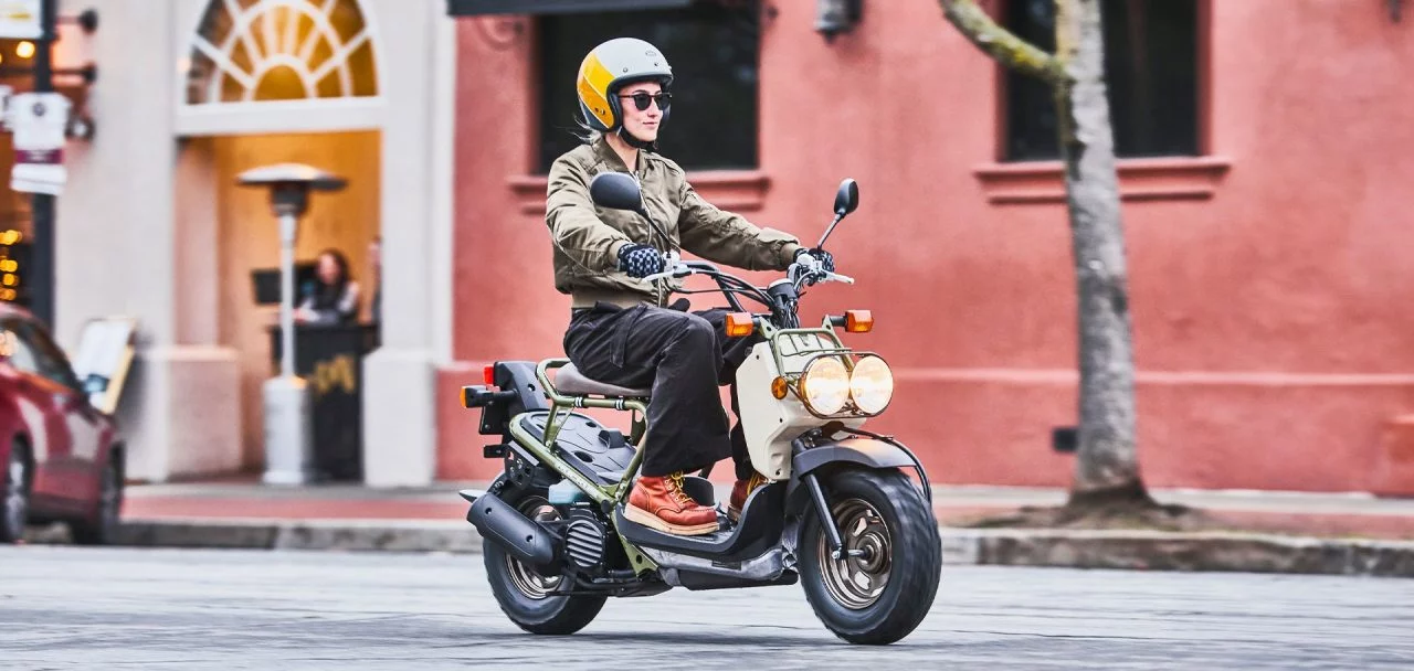 Vista lateral del Honda Ruckus 2025 en un entorno urbano, destacando su diseño audaz y compacto.