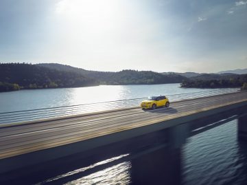 Vista lateral del Renault 5 eléctrico en entorno natural junto al lago.