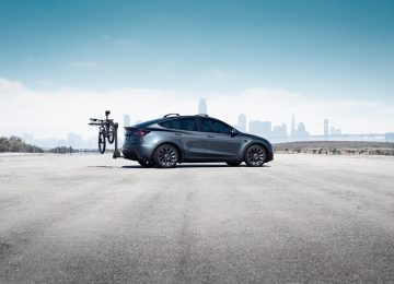 Vista lateral del Tesla Model Y con bicicleta en portabicicletas, trasfondo urbano.